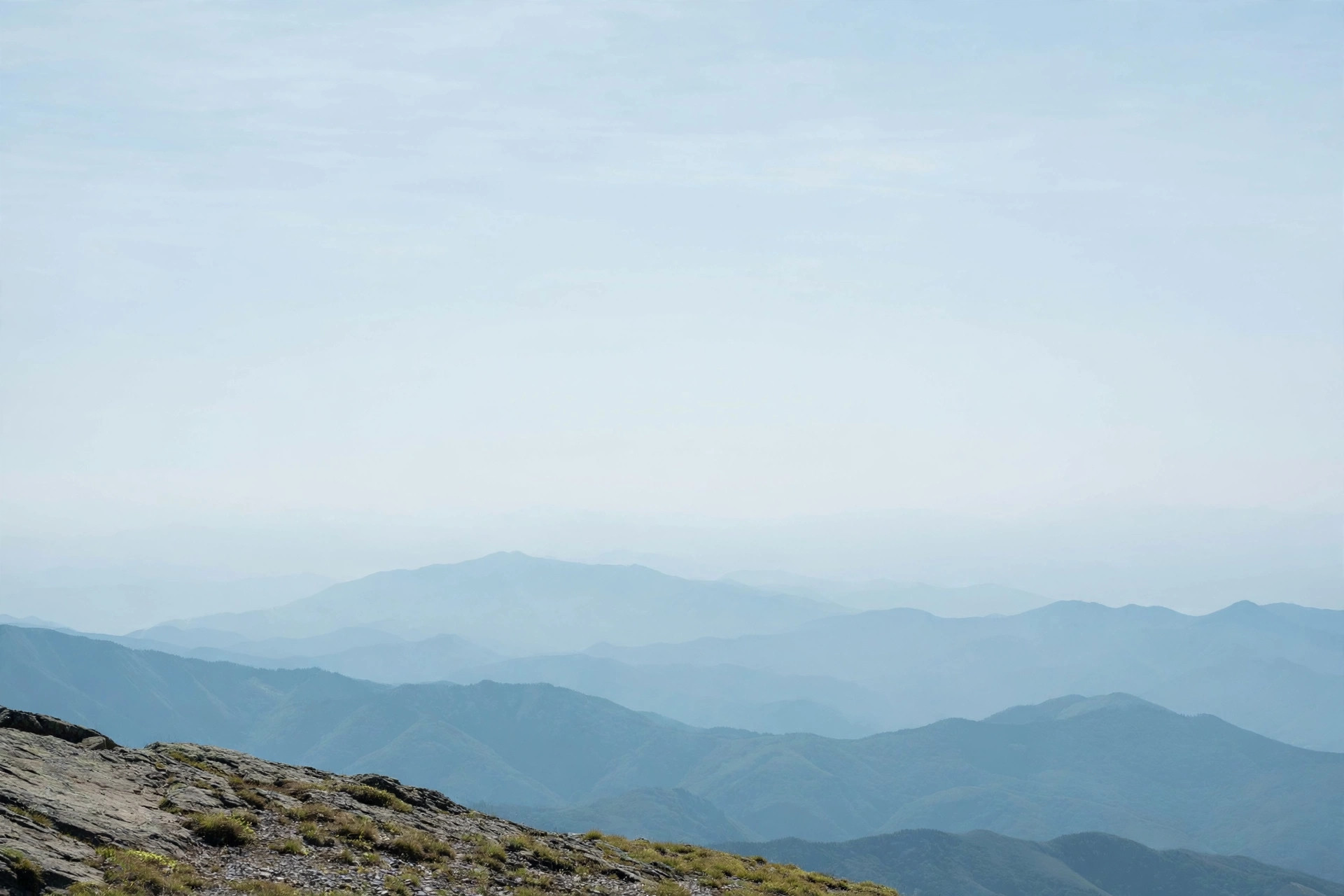 Distant mountain layers fading into soft blue haze under a vast summer sky